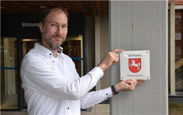 Jan Lubitz vom Landesamt für Denkmalpflege präsentiert das neu gestaltete Schild, dass das Kreishaus in Rotenburg als Denkmal ausweist.