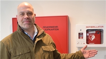 Mann zeigt auf Kasten mit Defibrillator