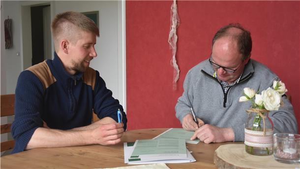 Das Foto zeigt den frischgebackenen Biobauern Jan Kaiser bei der Vertragsunterzeichnung. Daniel Bischoff, Erzeuger- und Umstellungsberater bei Bioland, schaut ihm dabei zu.  