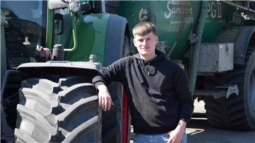 Junger Mann steht neben einem Traktor. 
