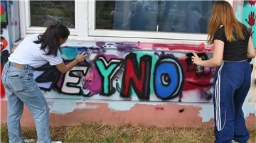 Zwei Mädchen sprayen an einer Wand