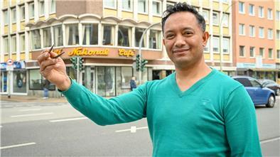 Ein Mann mit grünem Pullover hat zwei Essstäbchen in der Hand