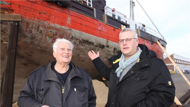Zwei Männer vor einem alten Schiff.