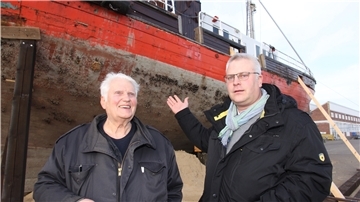 Zwei Männer vor einem alten Schiff.