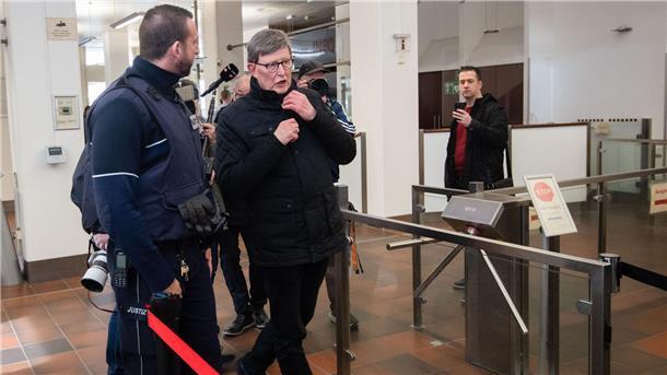Kardinal Rainer Maria Woelki wird im Foyer des Kölner Landgerichts von einem Justizbeamten (l) zur Sicherheitsschleuse begleitet.