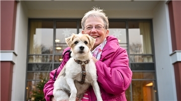 Frau mit Hund vor einem Haus