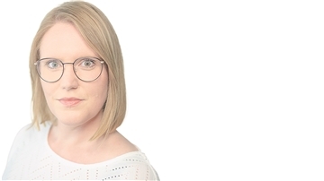 Blonde Frau mit dunkler Brille schaut direkt in die Kamera.