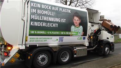 Ein großer Müllwagen hebt zwei braune Biotonnen zur Entleerung von der Straße hoch.