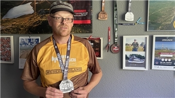 Mann mit Medaille um den Hals vor einer Wand mit weiteren Urkunden und Medaillen.
