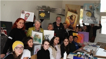 Schülerinnen halten ihre Bilder hoch, Erwachsene gucken zu