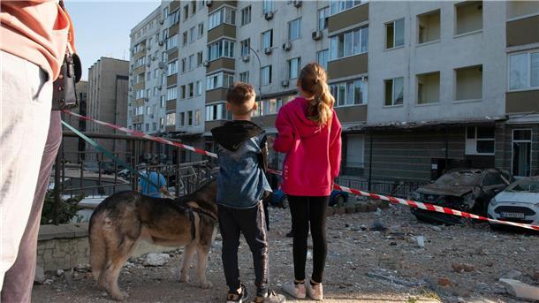 Kinder stehen vor kaputten Gebäuden in der Ukraine. Einige Kinder sollen bald Urlaub vom Krieg bekommen und dafür nach Deutschland reisen.