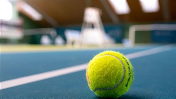 Elitär ist vorbei - so viel kostet der Tennissport wirklich Ein gelber Tennisball liegt auf blauem Teppichboden in einer Tennishalle.