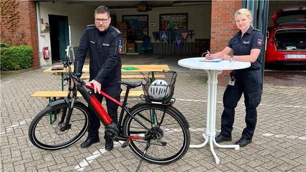 Eine Polizeibeamtin füllt an einem Stehtisch ein Formular aus, neben ihr untersucht ein Polizeibeamte ein Fahrrad.