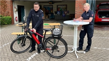 Eine Polizeibeamtin füllt an einem Stehtisch ein Formular aus, neben ihr untersucht ein Polizeibeamte ein Fahrrad.