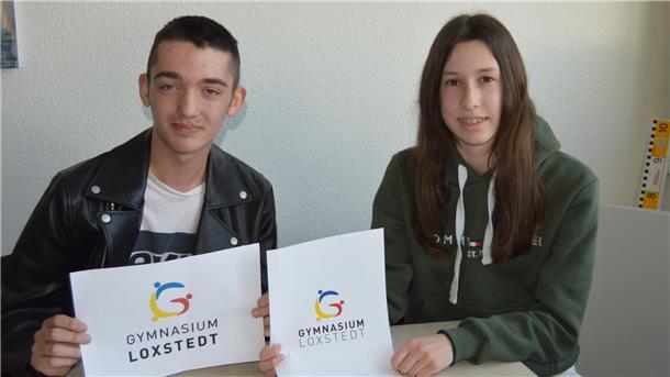 Schüler und Schülerin halten das auf Papier gedruckte neue Logo des Gymnasiums Loxstedt hoch