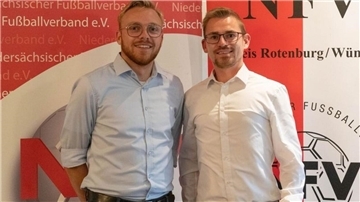 Zwei Männer in Oberhemden stehen vor einer rotweißen Stellwand.