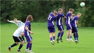 Ein Mann schießt einen Ball. Vier andere Männer springen in die Luft. 
