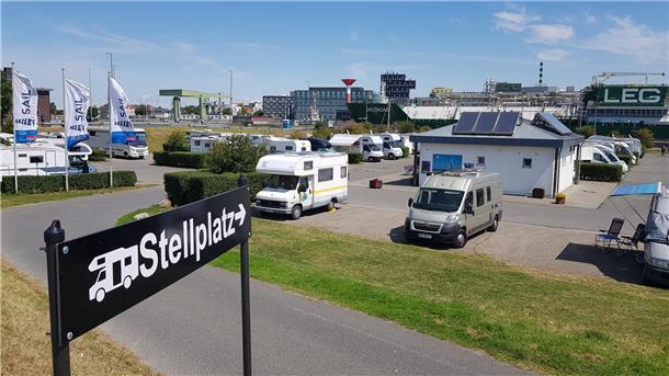 Ein Schild mit der Aufschrift "Stellplatz" steht vor einem Stellplatz für Wohnmobile. 