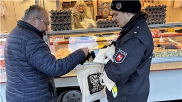 Kunde Günter Wilkens (links) nimmt aus den Händen von Polizeikommissar Fabian Ostrau eine Tasche entgegen. „Gewalt kommt nicht in die Tüte“ steht darauf.