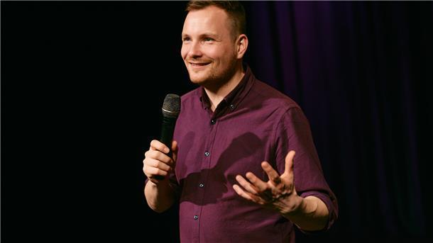 Ein Mann mit Mikro in der Hand auf einer Bühne. Kunsthistoriker und Comedian Jakob Schwerdtfeger liest im Rahmen des Literarischen Herbstes in der Stadtbibliothek Bremerhaven.