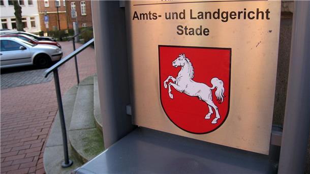 Ein Schild mit dem Niedersachsenpferd und der Aufschrift „Amts- und Landgericht Stade“ steht neben einem Treppenaufgang.