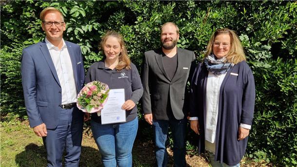 Wiebke Mayer-Reinecke: Neue Glücksbringerin für Nordenham-Mitte Vier Menschen stehen vor einer grünen Hecke. Landrat Stephan Siefken beglückwünscht Wiebke Mayer-Reinecke zu ihrer neuen Aufgabe als Bezirksschornsteinfegermeisterin.