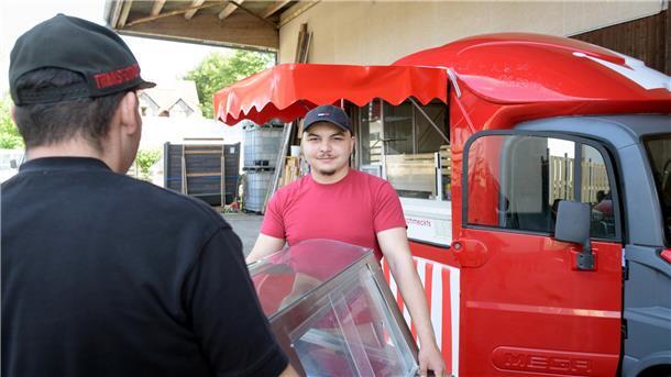Leandro startet auf der Sail als Schausteller Zwei Männer tragen eine Kühlvitrine zu einem roten Foodtruck