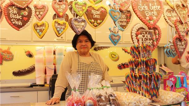 Frau steht in ihrem Stand. Um sie herum sind Lebkuchenherzen