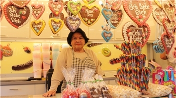 Frau steht in ihrem Stand. Um sie herum sind Lebkuchenherzen