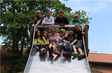 Kinder sitzen mit ihrer Lehrerin auf einer Rutsche.