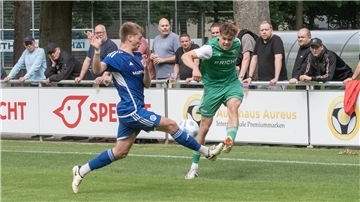 Zwei Männer kämpfen um einen Ball und mehrere Männer gucken im Hintergrund zu.