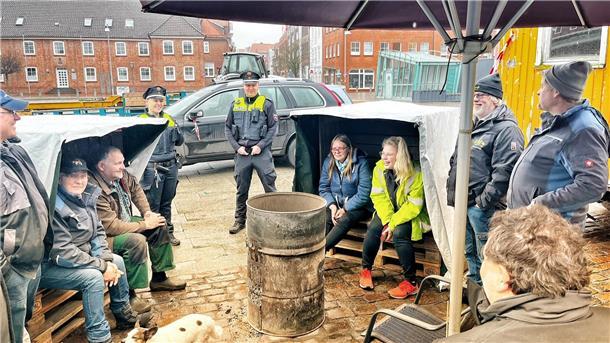 Campteilnehmer und zwei Polizisten stehen oder sitzen rund um die Feuertonne
