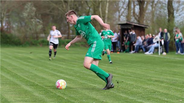 Ein Mann in einem grünen Trikot läuft hinter einem Ball her.