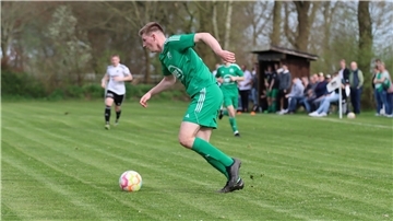 Ein Mann in einem grünen Trikot läuft hinter einem Ball her.
