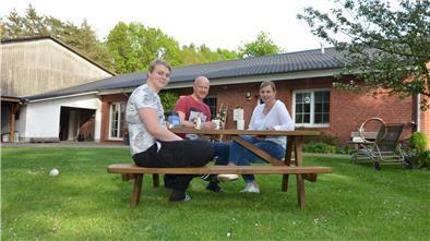 Madlen und Thomas Kühl sitzen mit ihrem Sohn Louis im Garten vor dem Haus der Familie. Die Immobilie wurde 2020/21 energetisch saniert und wurde dafür mit der Grünen Hausnummer ausgezeichnet.