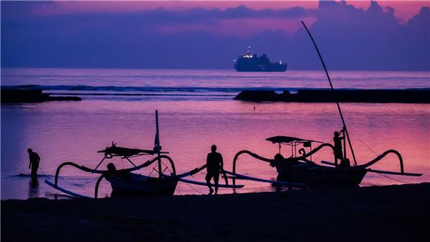 Männer befestigen vor Sonnenaufgang am Tag vor Beginn des G20-Gipfels am Strand von Nusa Dua Boote. Im Hintergrund ist ein Schiff der indonesischen Marine zu sehen.