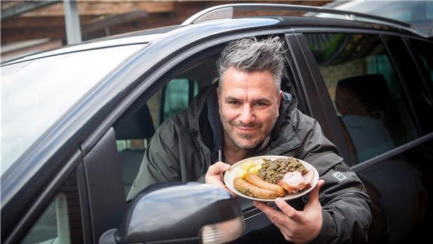 Marco Tienz, Grünkohltaxi-Betreiber, sitzt mit einem Grünkohlteller in seinem Auto.