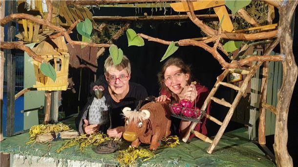 Zwei Frauen in der Kulisse eines Puppenspiels mit Puppen einer Kuh und einer Krähe