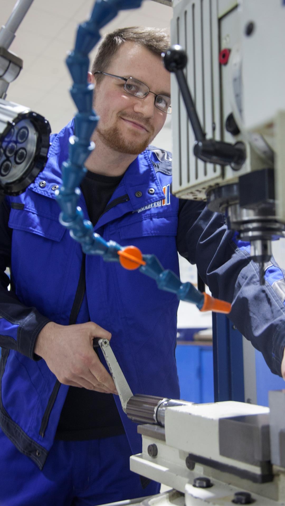 Ein Mann in blauer Arbeitskleidung steht an einer Maschine. 