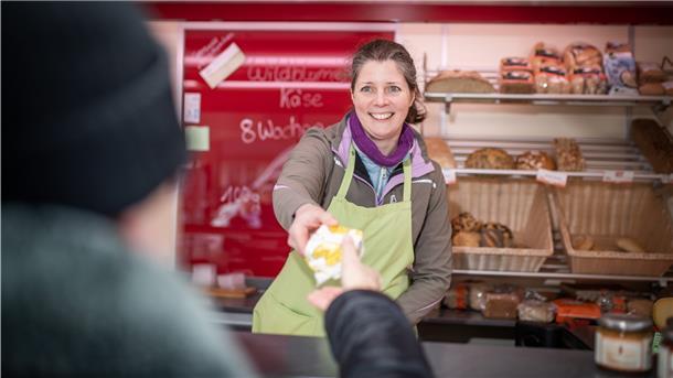 Eine Frau reicht Käse über eine Verkaufstheke. 