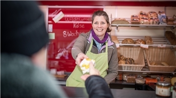 Eine Frau reicht Käse über eine Verkaufstheke. 