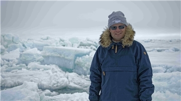 Ein Mann mit Parka, Mütze und Sonnenbrille steht im Ewigen Eis. 