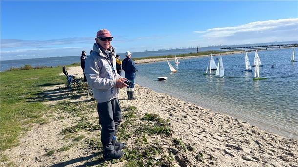 Leute stehen am Strand und navigieren ihre Modellsegelboote per Fernsteuerung