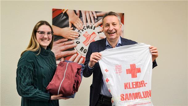 Eine junge Frau und ein Mann halten einen Kleidersack und lächeln in die Kamera.