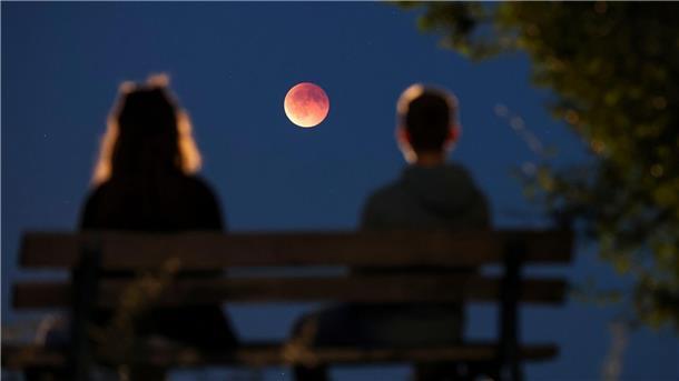 Bilder des Tages Menschen betrachten von einer Parkbank aus die auch als Blutmond bezeichnete totale Mondfinsternis in Leipzig.