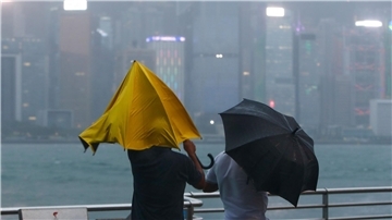 Menschen mit Regenschirmen kämpfen in Hongkong gegen starken Wind und Regen des Taifuns „Saola“ an.