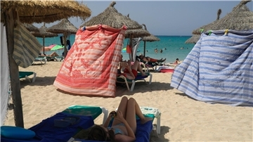 Menschen schützen sich bei extremer Hitze mit Strandtüchern vor der Sonne am Strand von Arenal.