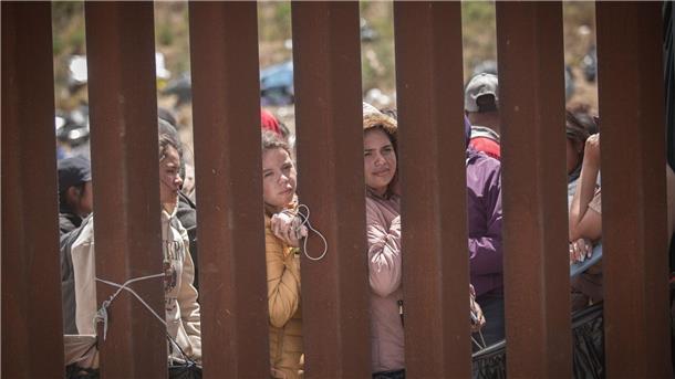 Menschen stehen hinter der Grenzmauer zwischen Mexiko und USA und hoffen darauf, in die USA einreisen zu können.