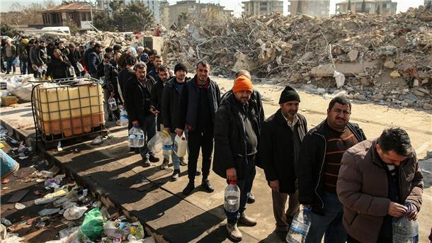 Hoffnung und Trauer: Erschöpfte Helfende in der Türkei Menschen stehen neben eingestürzten Gebäuden an, um Wasser zu holen.