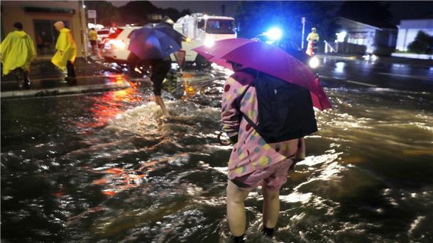 Menschen überqueren eine überflutete Straße. Nach massiven Regenfällen stehen weite Teile Aucklands unter Wasser.